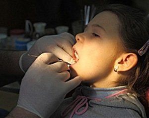 Врач-стоматолог проводит осмотр ротовой полости ребенка